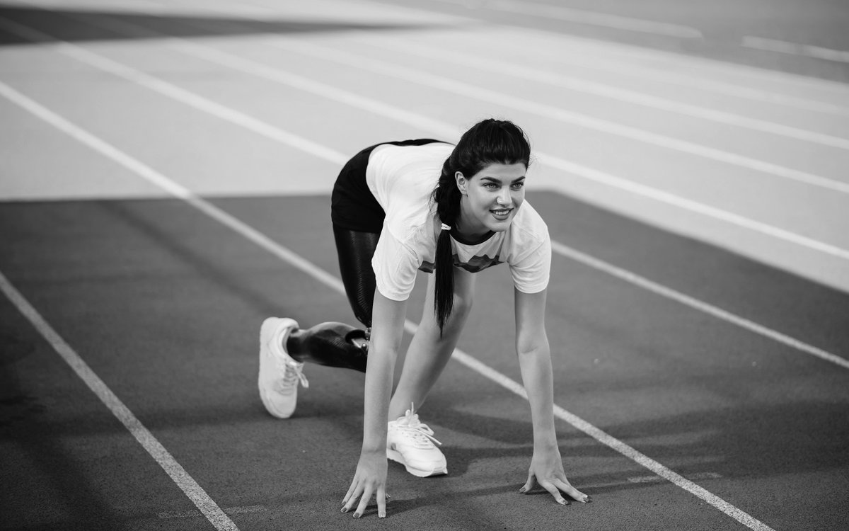 Eine Frau mit Beinprothese ist in Startposition auf einer Laufstrecke in einer Sportanlage.